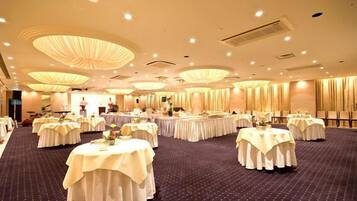 Un salón de banquetes con mesas redondas cubiertas con manteles blancos, dispuesto en un espacio amplio.