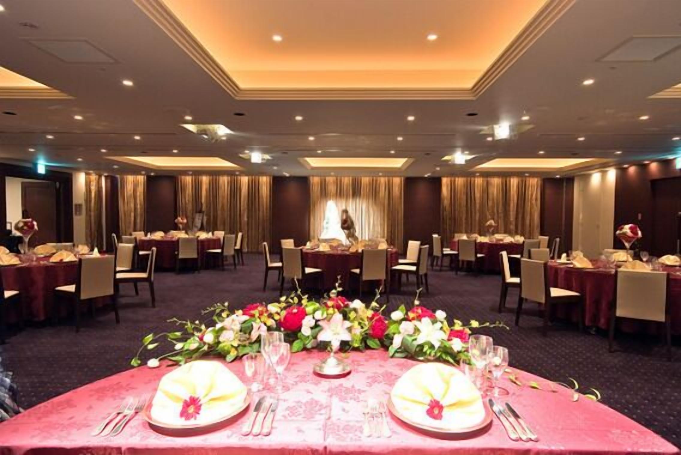 A banquet hall with round tables set for dining, a central floral arrangement, and a chandelier.