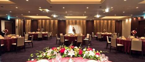 A banquet hall with round tables set for dining, a central floral arrangement, and a chandelier.