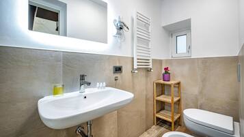 Un baño moderno con un lavamanos blanco, un inodoro, una bañera, un perchero para toallas y un ventanal pequeño.