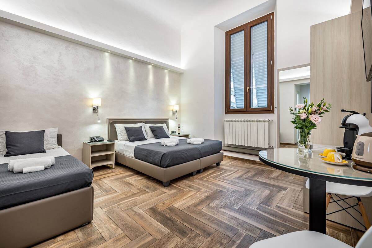 Une chambre d’hôtel moderne avec deux lits, une table à manger en verre, une machine à café et une vue sur la ville.