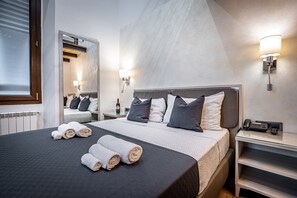 Une chambre d’hôtel moderne avec un grand lit, deux tables de chevet, un miroir et des lampes fixées au mur.