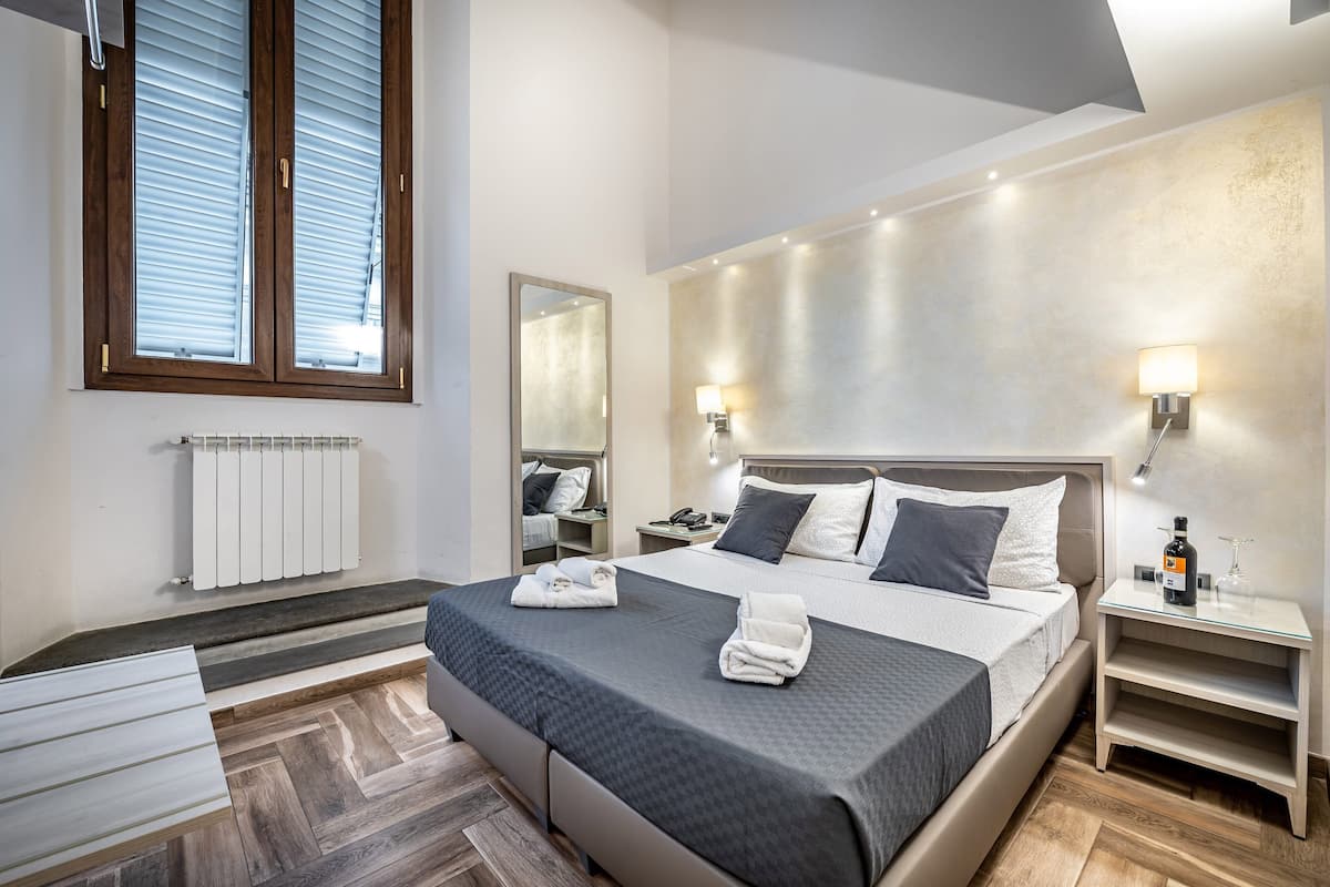 Une chambre d’hôtel moderne avec un grand lit, des tables de chevet, un miroir et un radiateur.