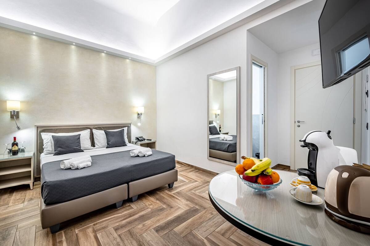 Une chambre d’hôtel moderne équipée d’un lit, de tables de chevet, d’un miroir, d’une télévision et d’un coin pour prendre le petit-déjeuner.