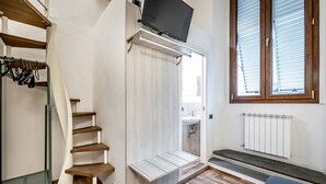 A bedroom with a wooden staircase, a built-in bench, a TV mounted on the wall, a window with blinds, and a radiator. - B&B Lorenzo de' Medici (Florence)