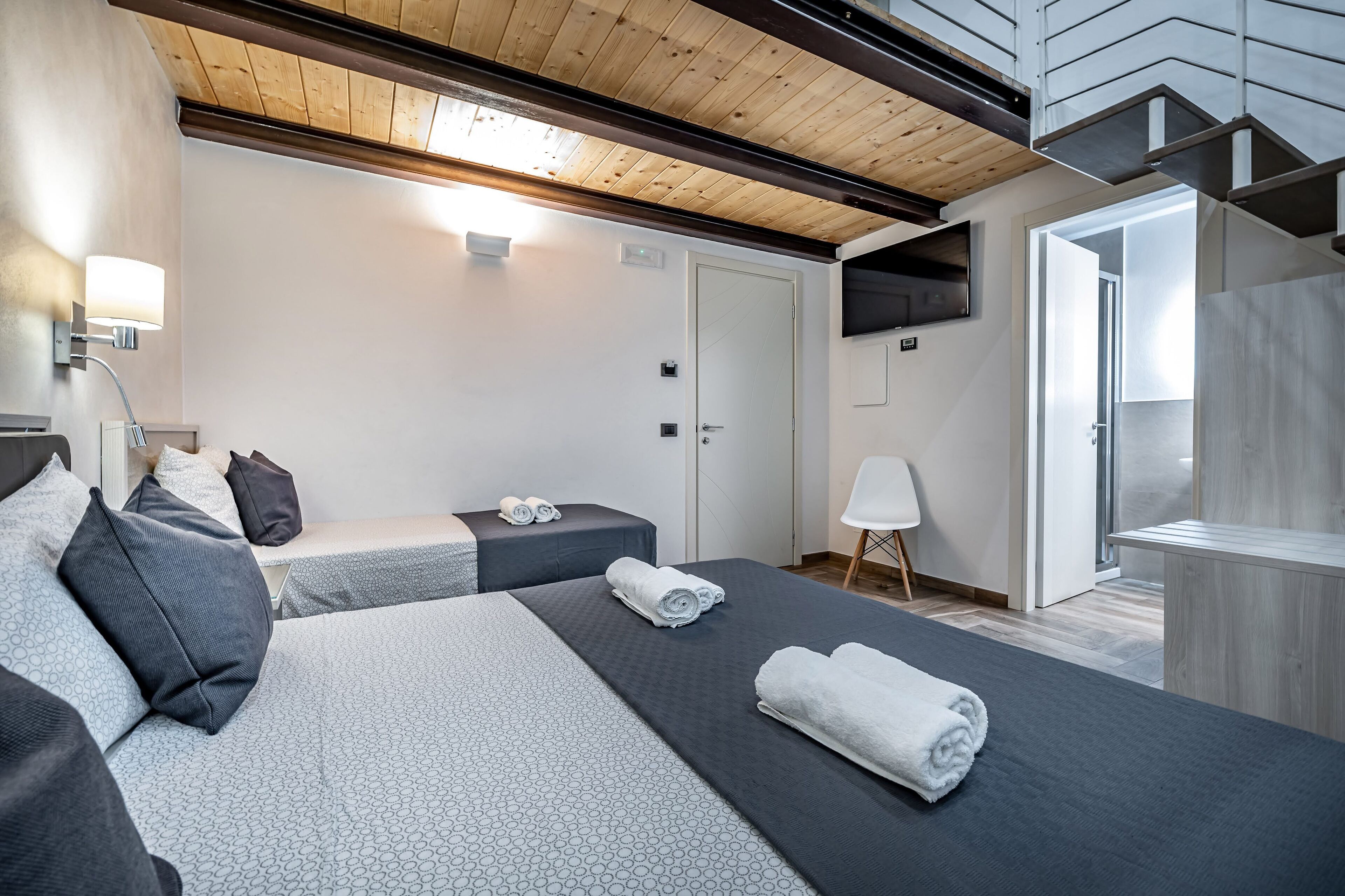 Una habitación de hotel moderna con dos camas, techo de madera, televisor y vista al exterior.