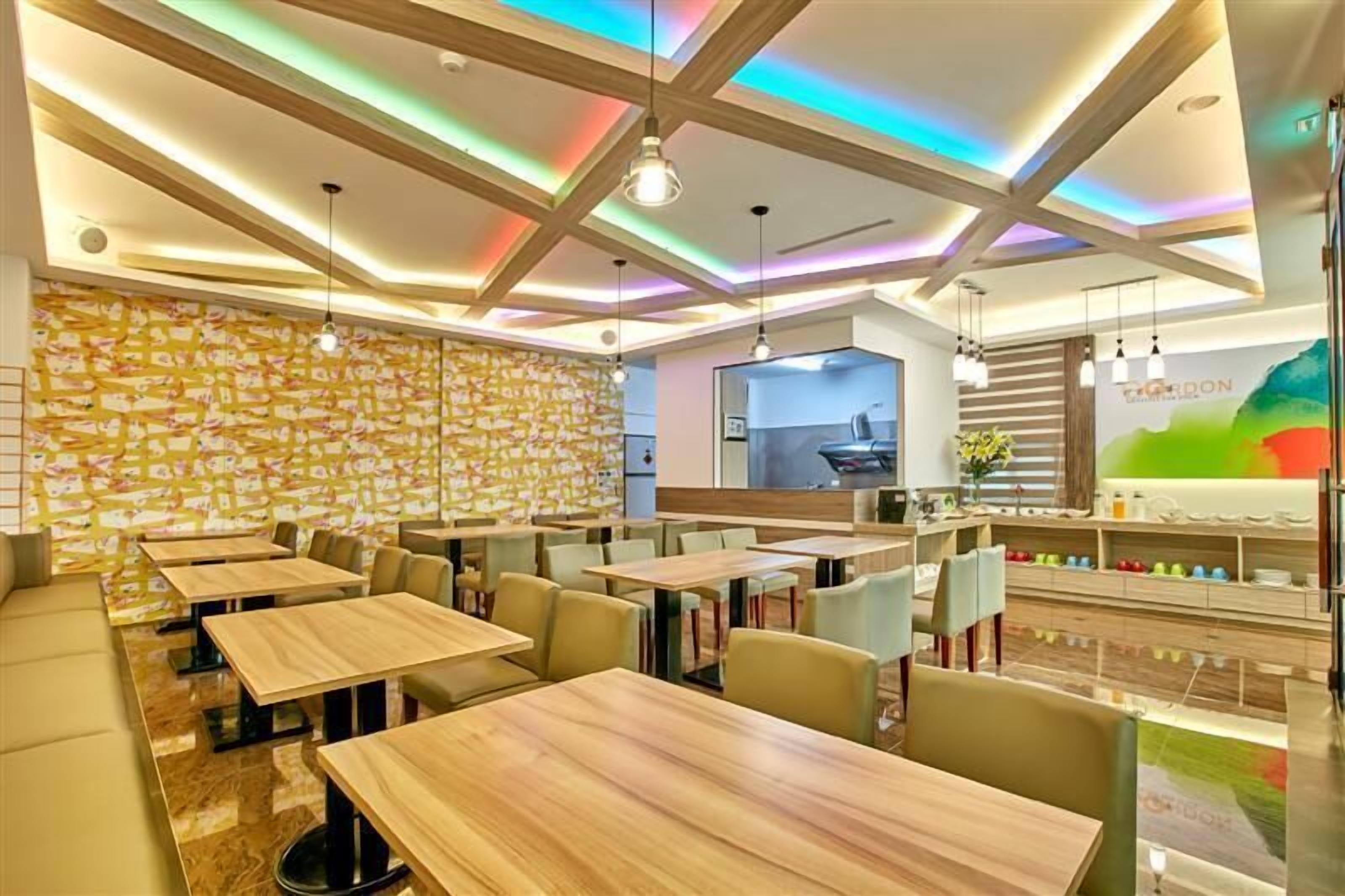 L’intérieur d’un restaurant moderne, avec des tables et des chaises en bois, un plafond aux couleurs vives et un comptoir orné d’une enseigne « Cordon ».