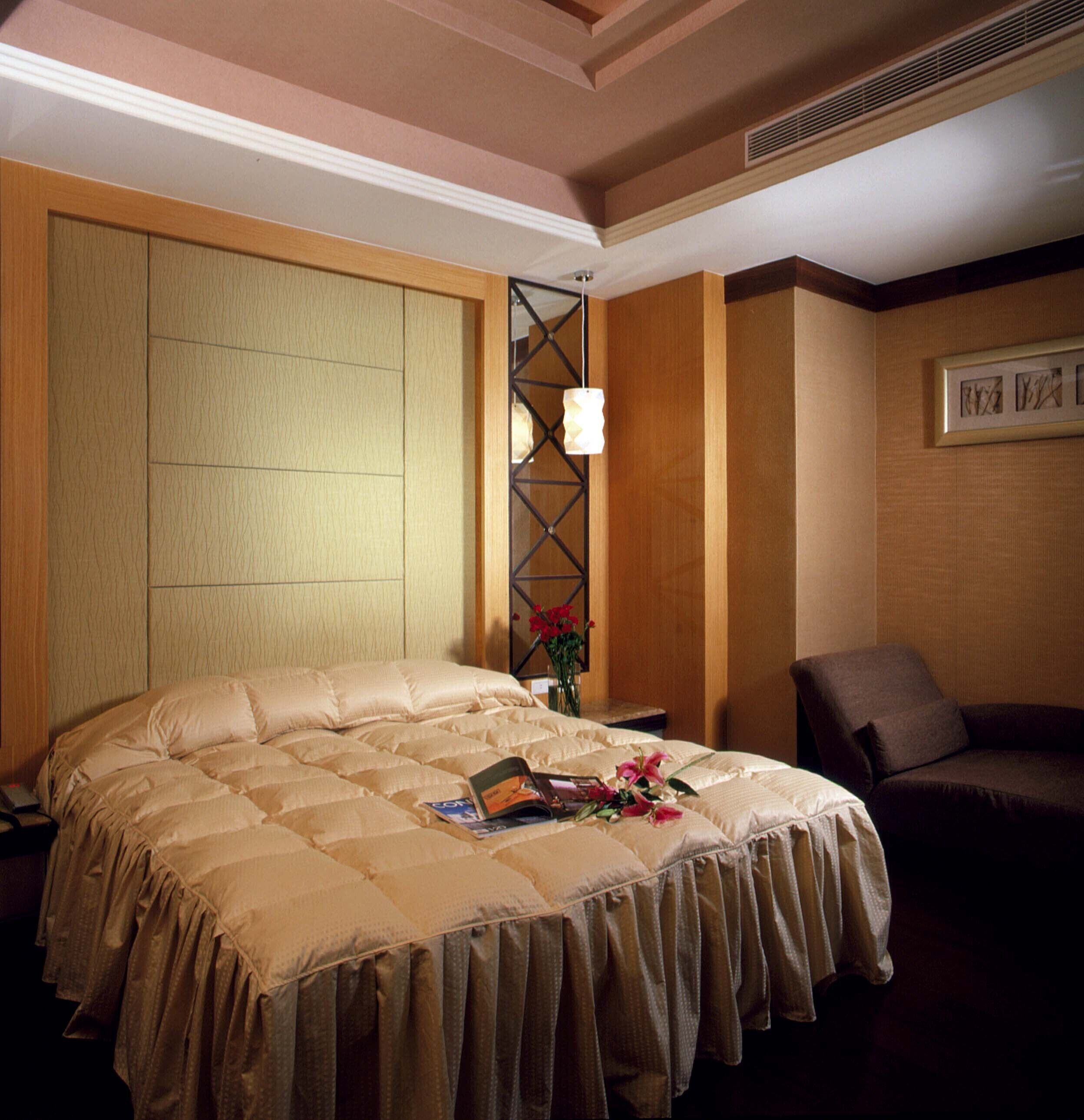 A hotel room with a large bed, a nightstand, a chair, and a wall-mounted light fixture.