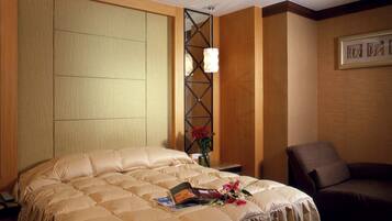 A hotel room with a large bed, a nightstand, a chair, and a wall-mounted light fixture.