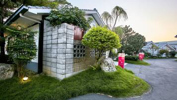 Un edificio moderno con fachada de piedra, un pequeño jardín con césped y un árbol, y un camino de entrada pavimentado.