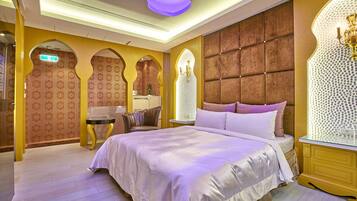 A hotel room with a large bed, a vanity with a mirror, and a seating area with a table and chairs.