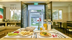 A breakfast buffet with various dishes, a vase with flowers, and a view of the garden through the open door. - Gold Motel (Puxin)