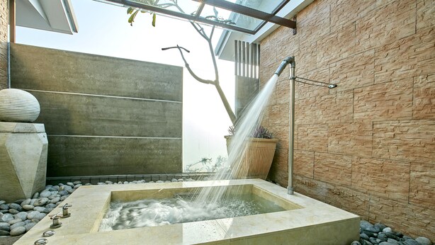 A modern outdoor hot tub with a stone wall backdrop, a water feature, and a tree. - Gold Motel (Puxin)