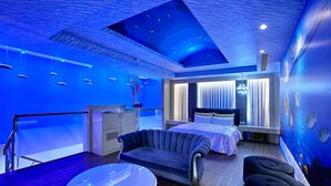 A modern hotel room with a blue-themed ceiling, a bed, a sofa, and a round table. - Gold Motel (Puxin)