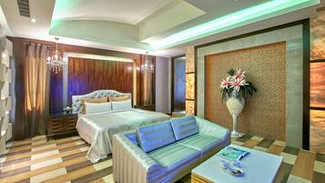 A modern hotel room with a large bed, a sofa, a coffee table, and a decorative plant.