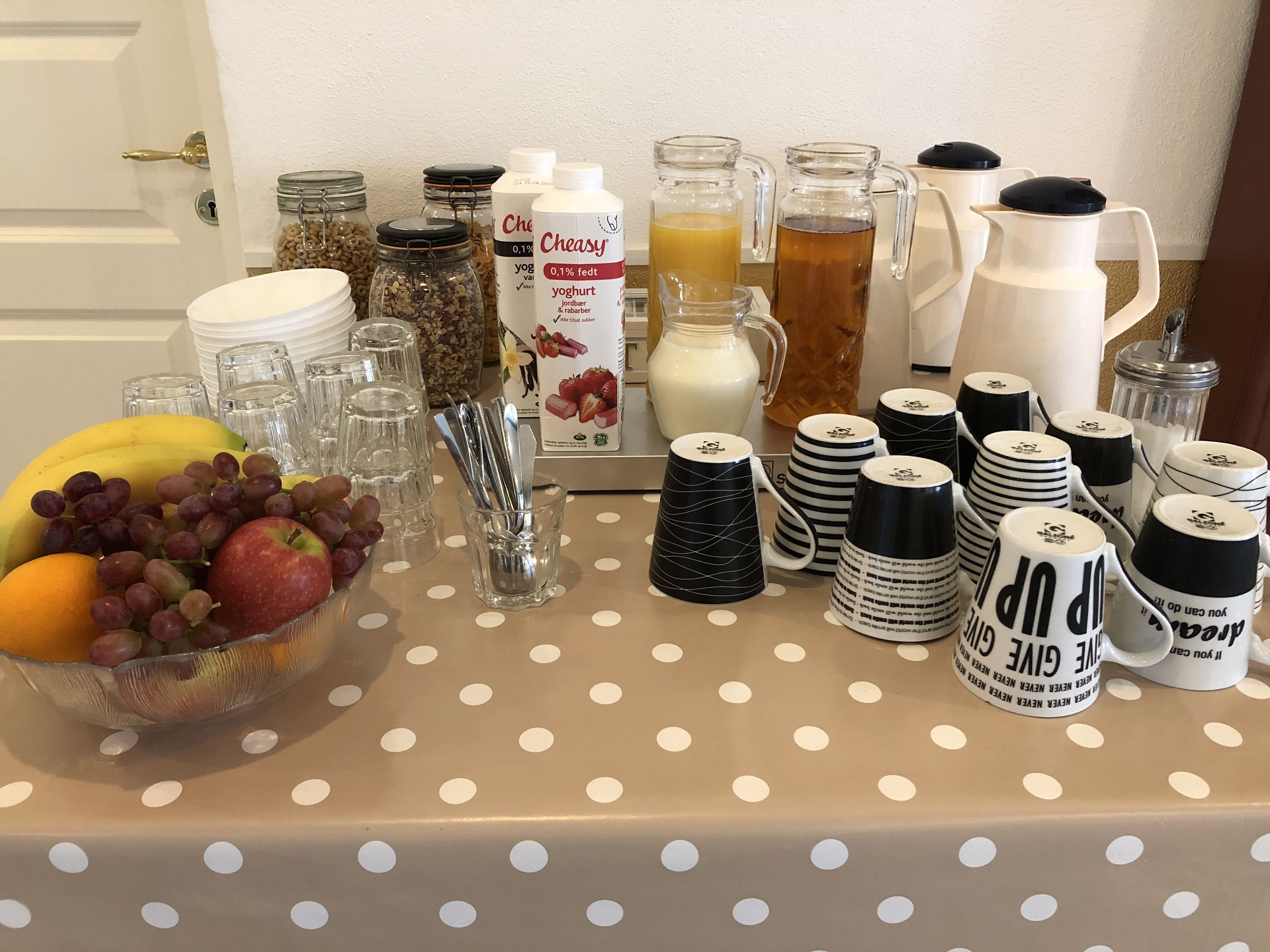 A table with a polka dot tablecloth, a bowl of fruit, and various kitchen items including jars, bottles, and mugs.