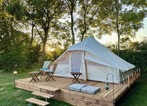 Una carpa con una terraza, dos sillas, una mesa y un farol.