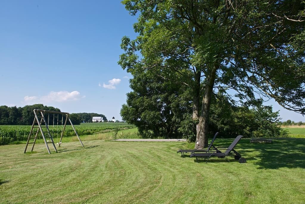 A grassy outdoor area with a swing set and two lounge chairs under a large tree.