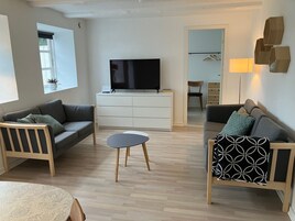 En moderne stue med to sofaer, et sofabord, et fjernsyn og et skab.