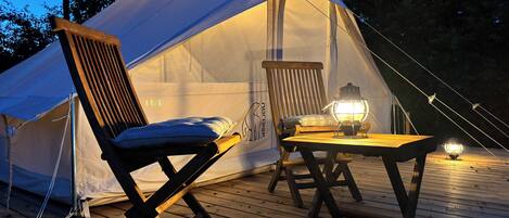 A tent with a table and chairs, a hanging chair, and a lantern on a wooden deck.