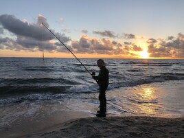 A person fishing by the sea during sunset.