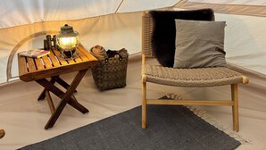 A tent interior with a wooden table, a lantern, a woven chair, and a grey cushion. - Myregaard B&B & Apartments (Nexø)