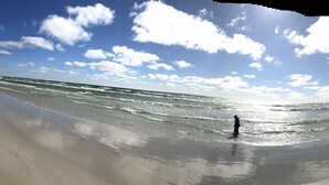 A beach with a lighthouse in the distance, a clear sky, and a person standing in the water. - Myregaard B&B & Apartments (Nexø)