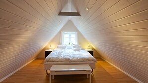 A narrow attic bedroom with wooden walls, a sloped ceiling, a bed, bedside tables, and a window. - Myregaard B&B & Apartments (Nexø)