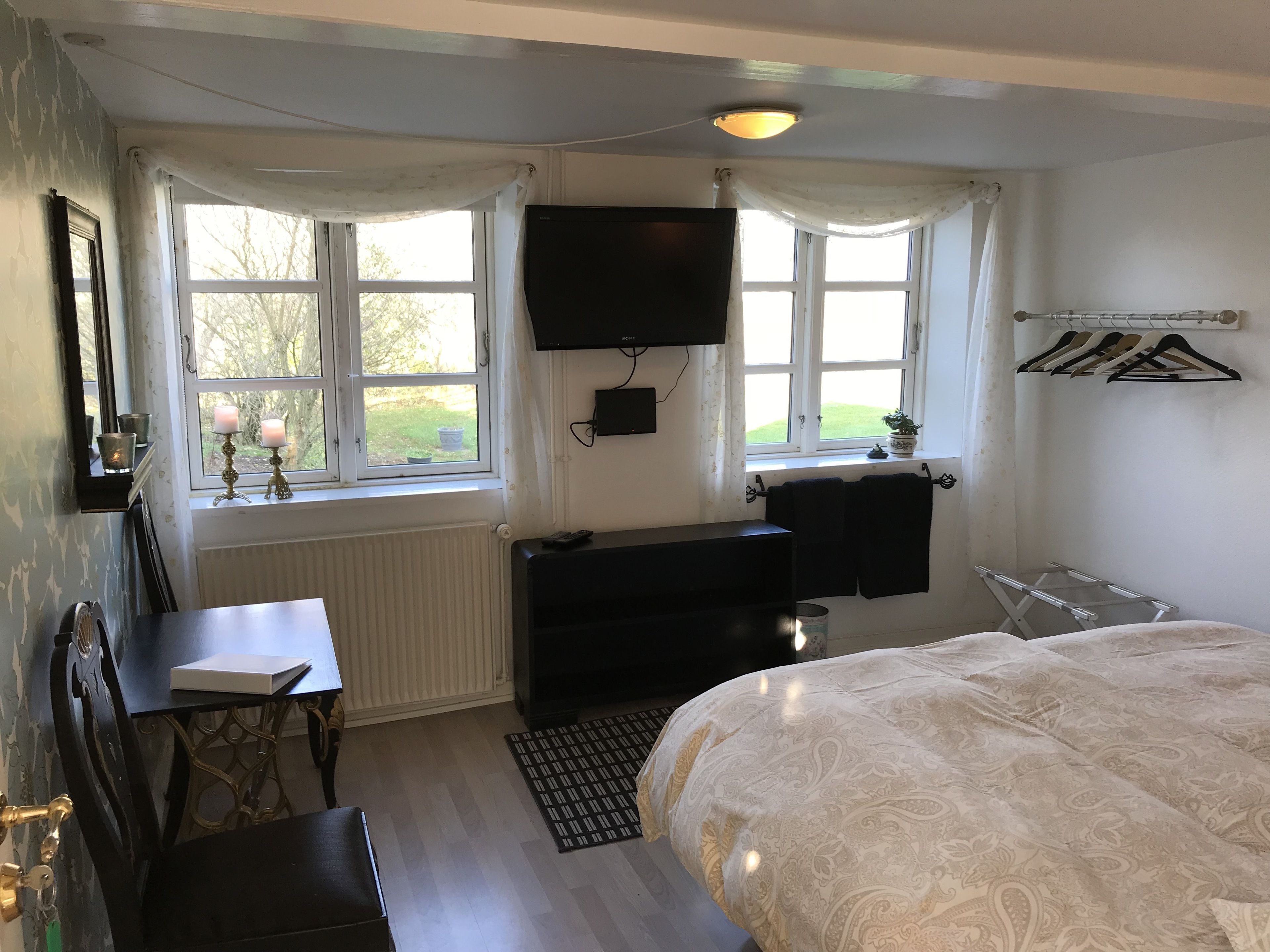 A bedroom with a bed, a desk, a chair, a radiator, a TV, and a window with curtains.