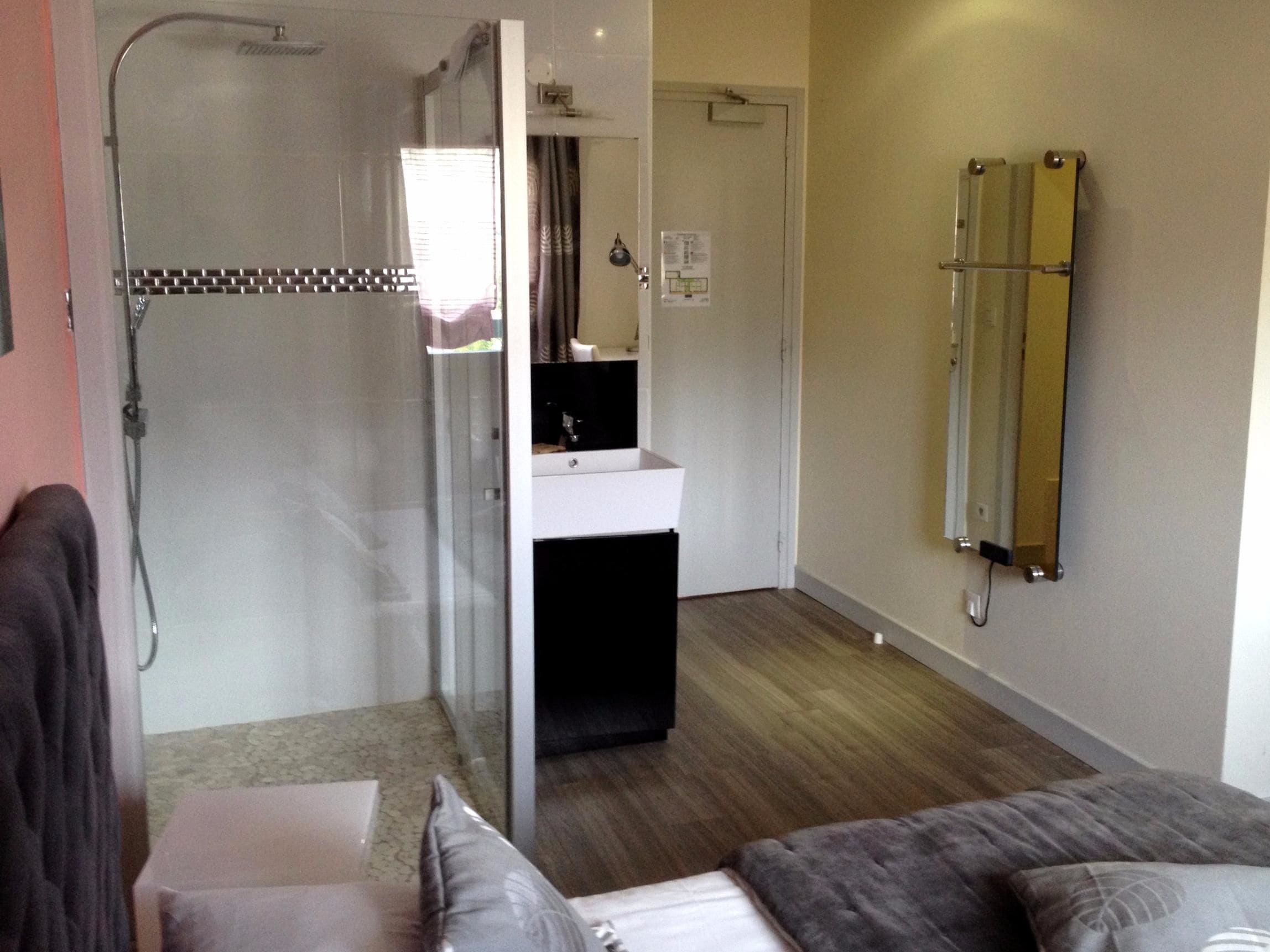 A hotel room with a shower, a sink, a mirror, and a bed with pillows.