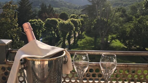 Una mesa metálica con una botella de champán y dos copas, frente a una vista panorámica de montañas.