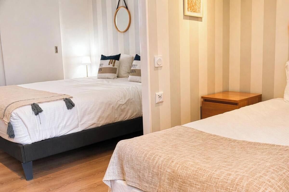 Two single beds with headboards, a small wooden nightstand, a wall-mounted mirror, and a light switch.
