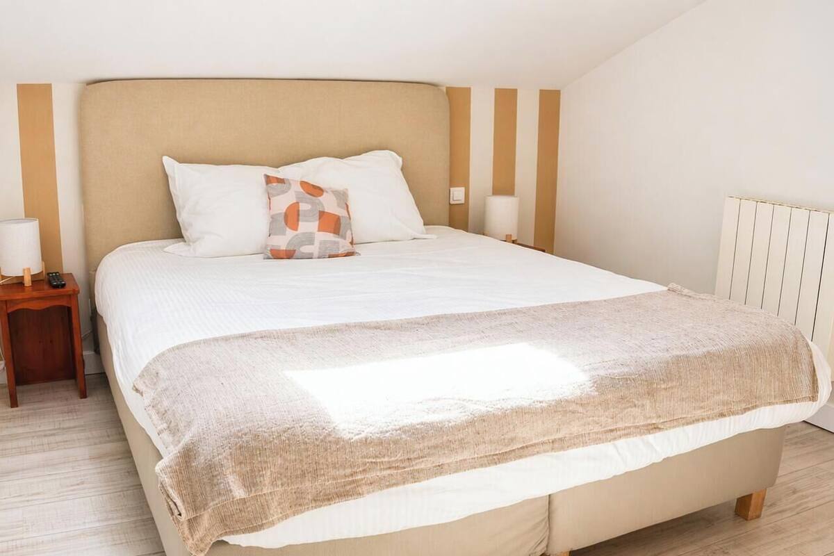A bedroom with a bed, pillows, a bedside table with a lamp, and a radiator.