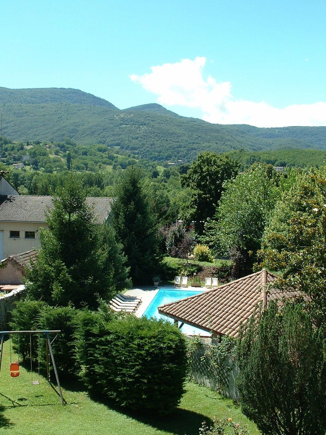 A residential area with a swimming pool surrounded by lush greenery and a view of distant hills.