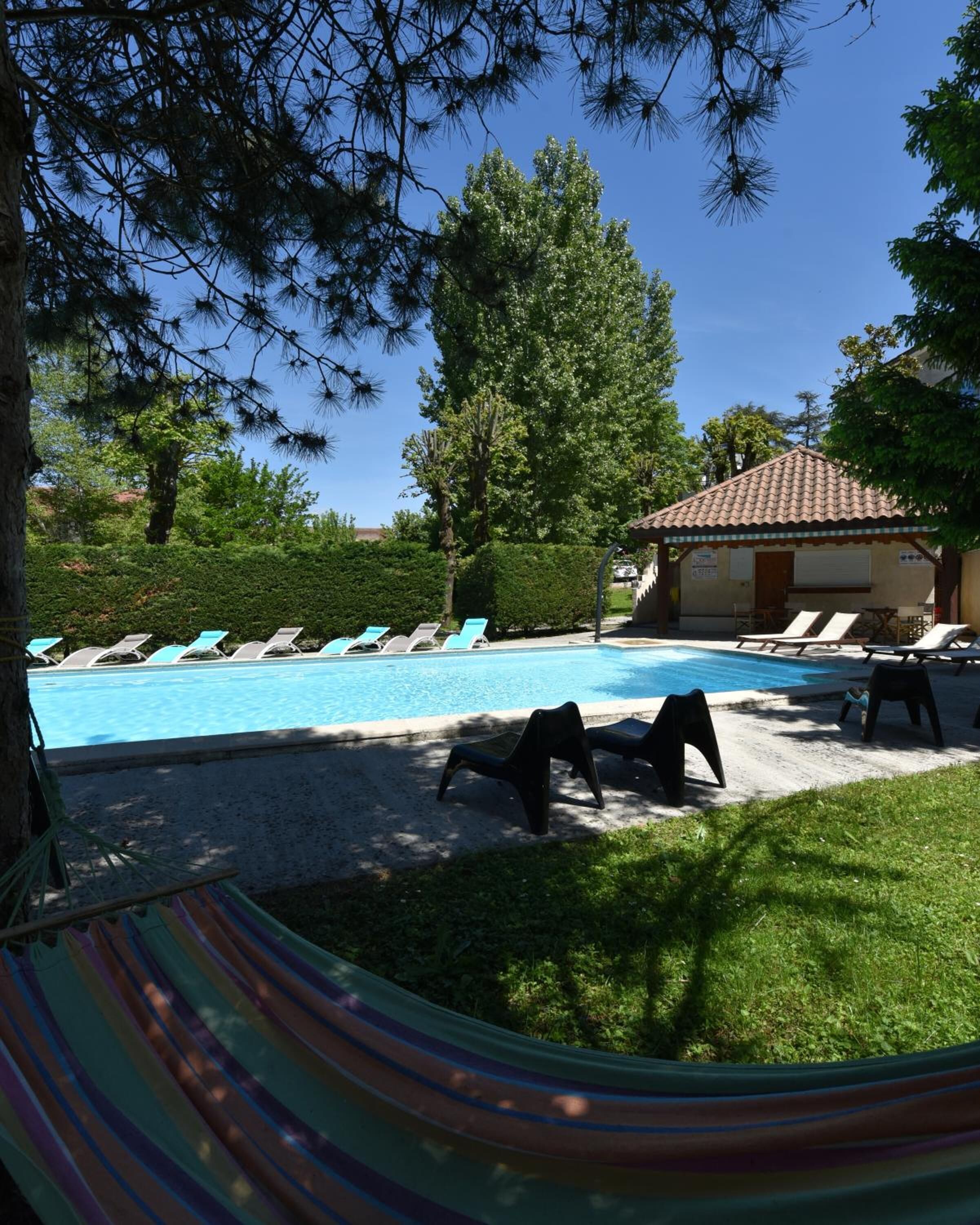 A pool area with lounge chairs and a small building with a tiled roof.