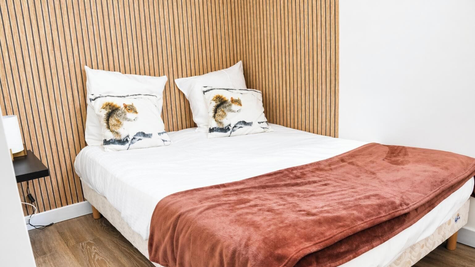 Un lit avec un matelas blanc, deux oreillers à motifs animaliers, une couverture marron et une tête de lit en bois à lattes.