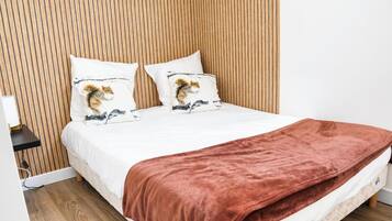 Un lit avec un matelas blanc, deux oreillers à motifs animaliers, une couverture marron et une tête de lit en bois à lattes.