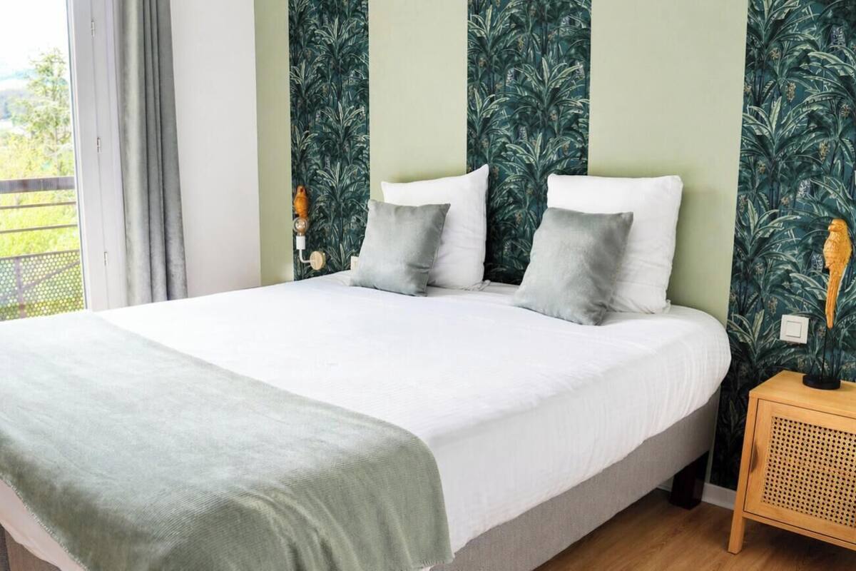 A bed with a green blanket, two pillows, and a wooden nightstand with a lamp.