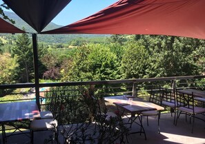 An outdoor patio with tables and chairs, a pool, and a view of a forested valley. - Logis Hôtel Restaurant Le Castel Fleuri (Saint-Jean-en-Royans)