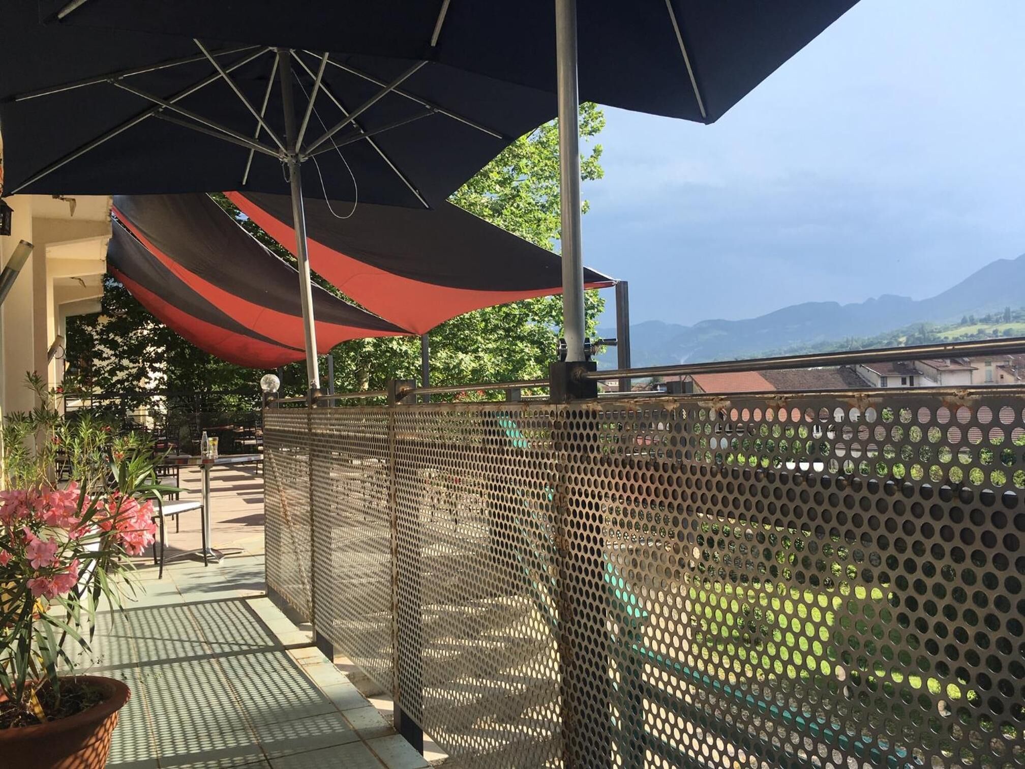 A balcony with a mesh fence, outdoor umbrellas, and a view of the mountains.