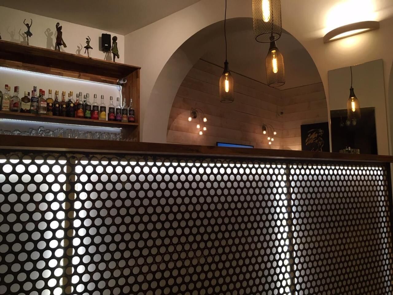 Eine Bar mit einer Holzauslage für Flaschen, einer Lochwand und hängenden Pendelleuchten.