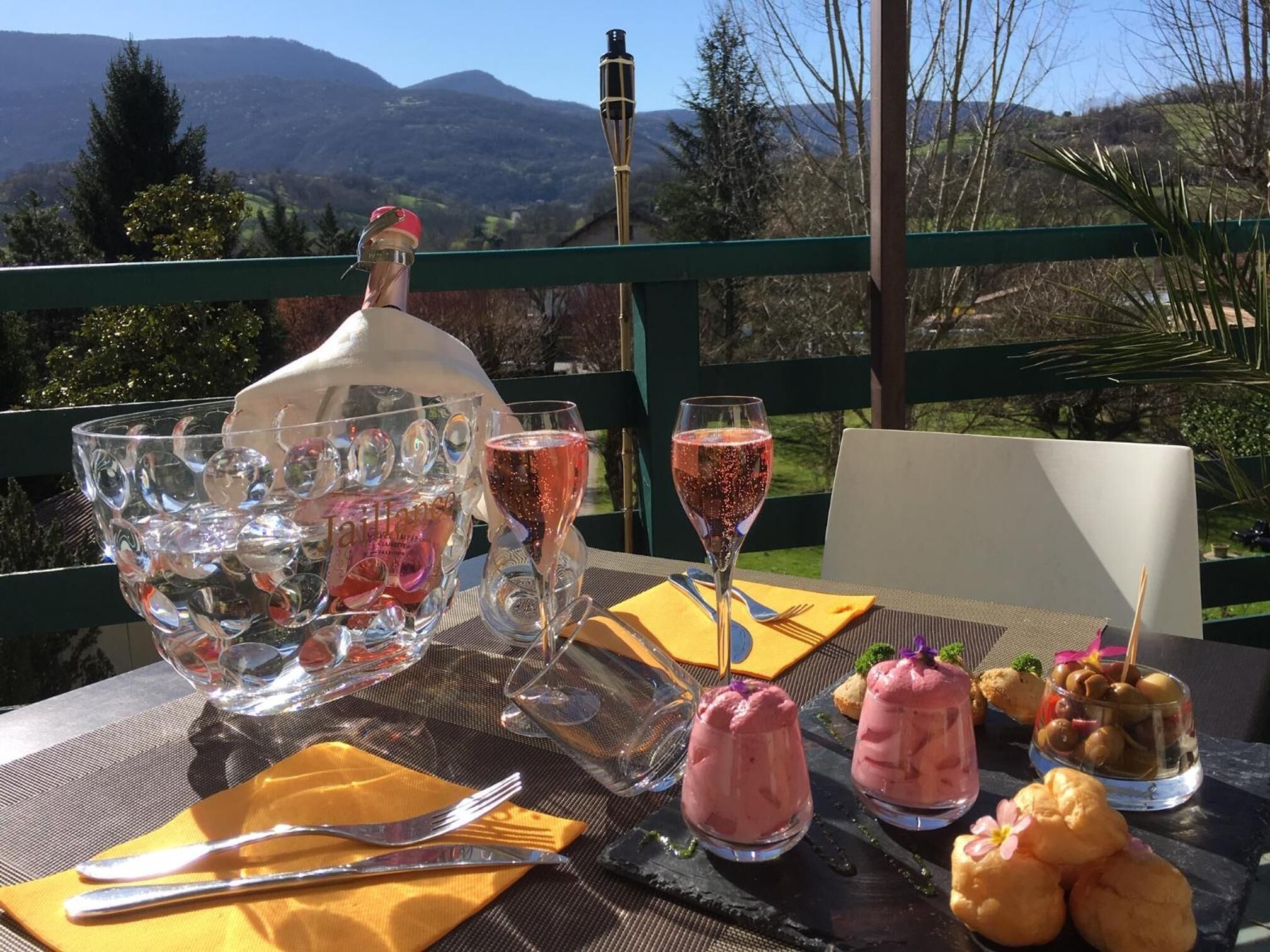 A table set outdoors with a bottle of sparkling wine, glasses, and a variety of desserts.