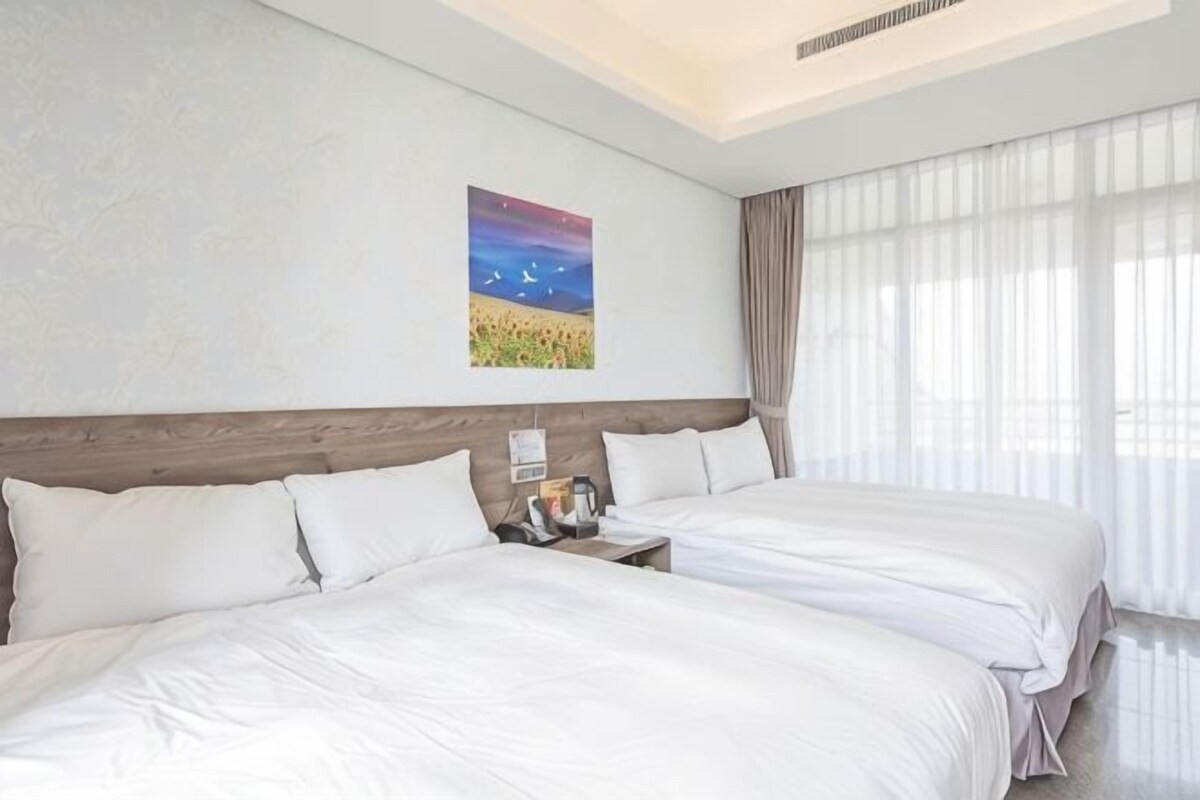A hotel room with two beds, a nightstand with a lamp, and a painting on the wall.