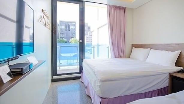 A hotel room with a bed, a desk, a TV, and a window with a view of buildings. - Hotel 99 (Taichung)