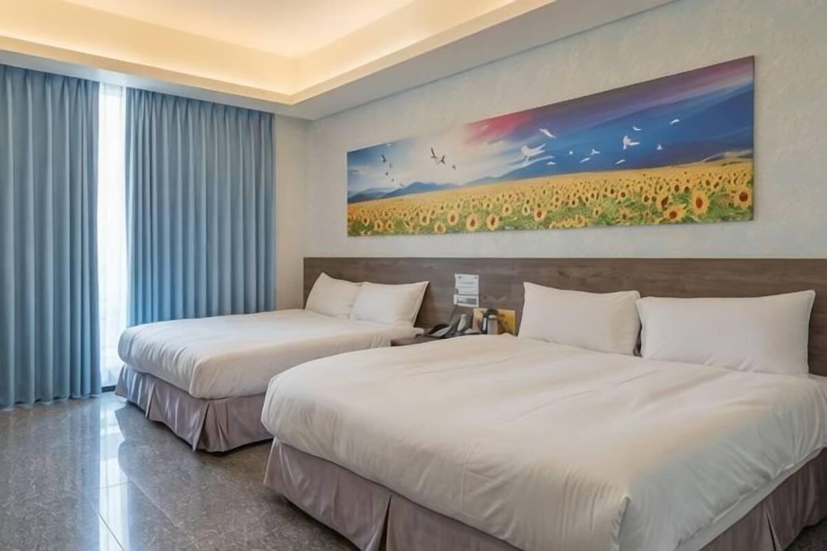 A hotel room with two beds, a painting of a field with birds, and a window with curtains.