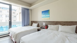 A hotel room with two beds, a wooden headboard, a painting of a beach, and a view of buildings through the window. - Hotel 99 (Taichung)