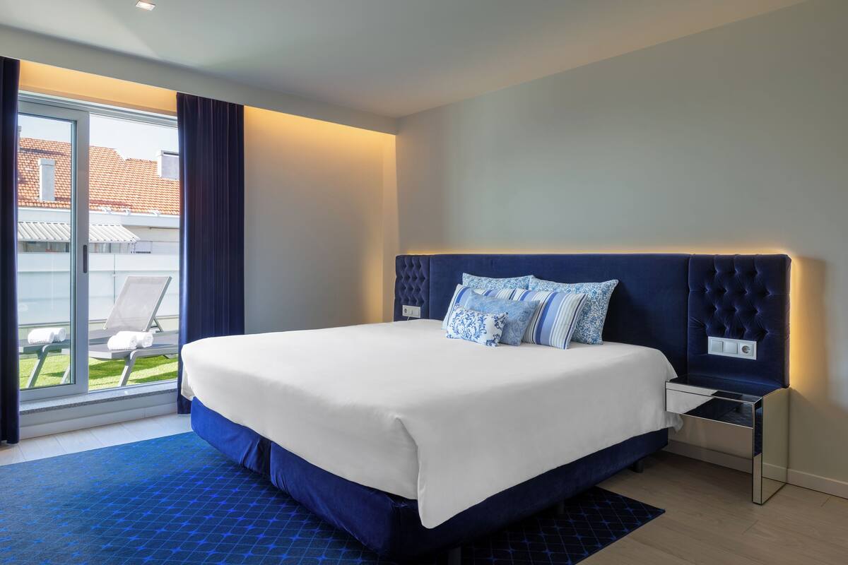 Ett modernt hotellrum med en stor säng, ett nattduksbord och utsikt över omgivningarna.