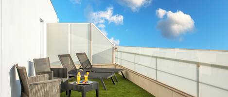 Een dakterras met rieten stoelen, een tafel met drankjes en een glazen balustrade.