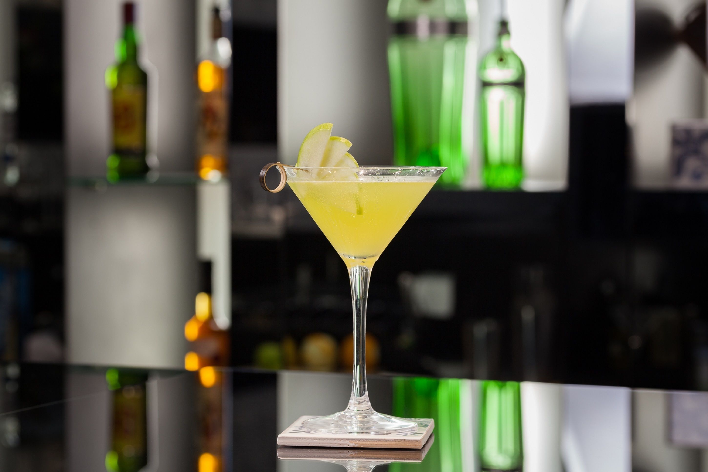 A martini glass with a lemon garnish on a reflective surface.