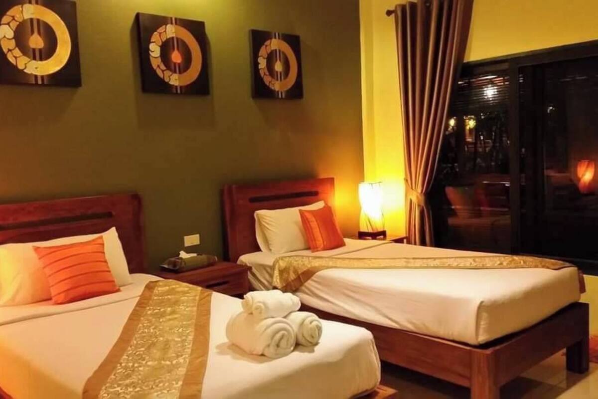Habitación de hotel con dos camas, una mesita de noche con lámpara y una ventana con cortinas.